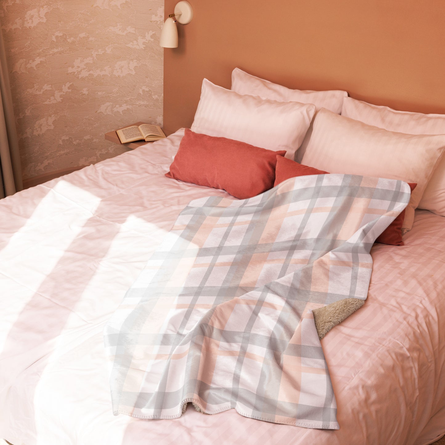 Peach grey plaid sherpa blanket draped over a bed with pink bedding and red pillows