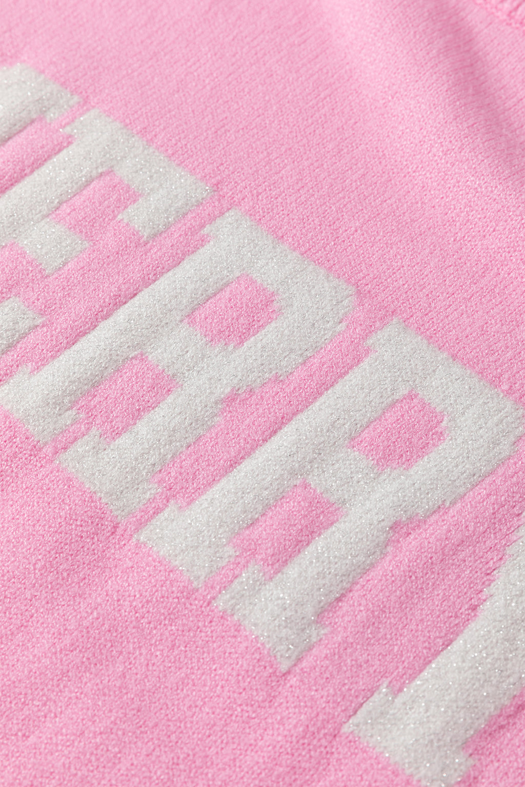 Close-up of a white MERRY Christmas sweater featuring a pink background and bold lettering