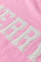 Close-up of a white MERRY Christmas sweater featuring a pink background and bold lettering