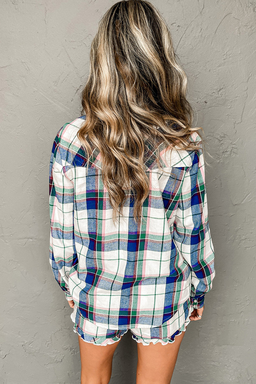 Woman wearing a plaid shirt with stylish ruffled shorts, showing a relaxed back view.