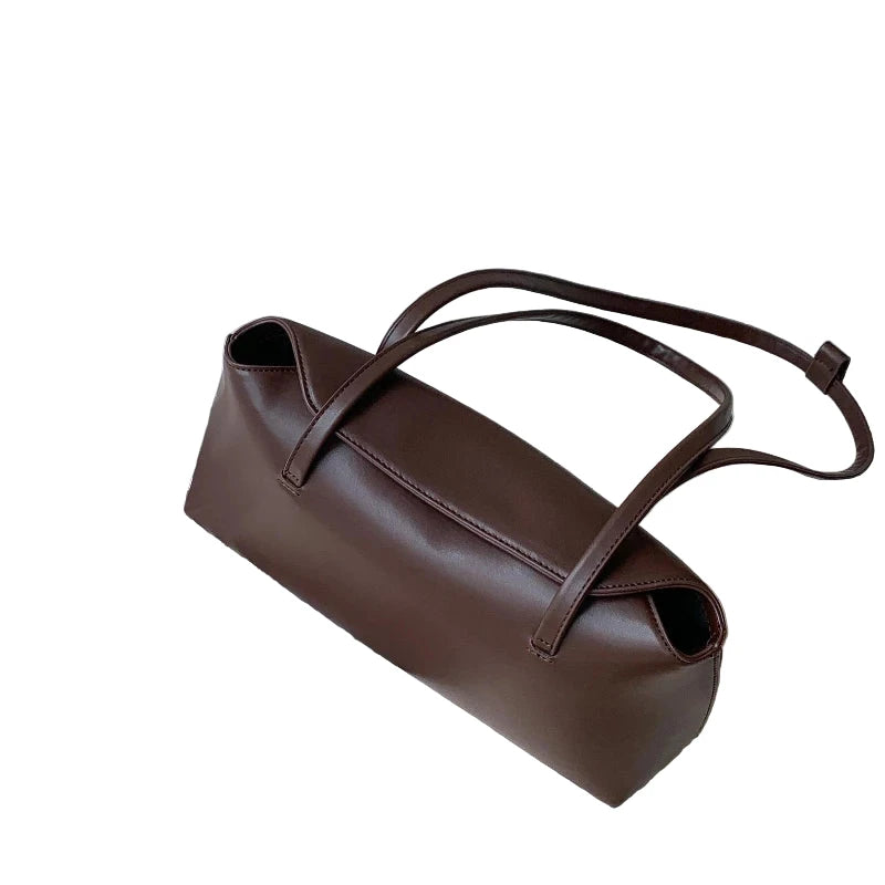 Stylish brown PU baguette shoulder bag for women placed on an open book next to a white wallet