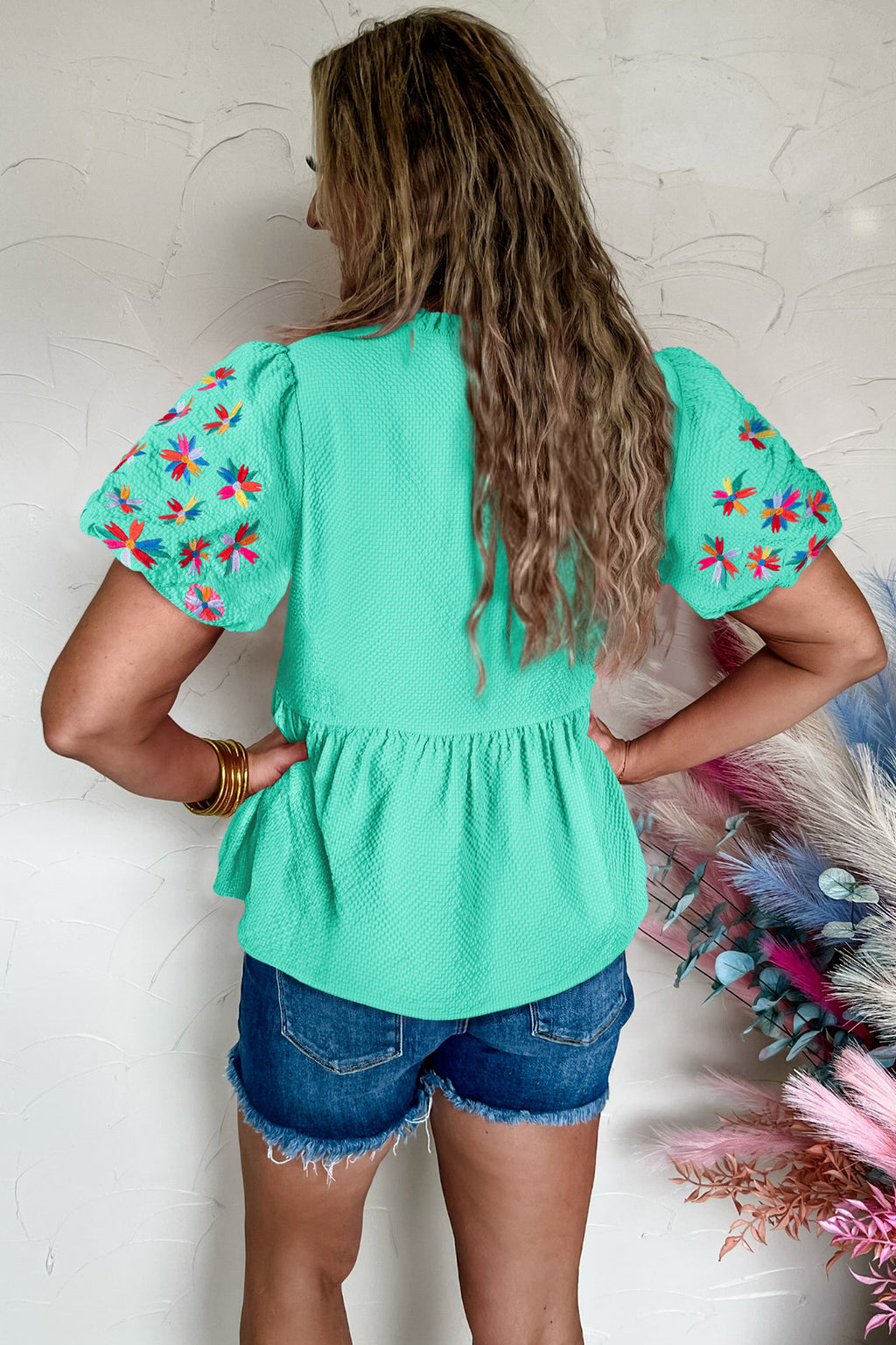 Back view of a mint green puff sleeve blouse with floral embroidery, paired with denim shorts