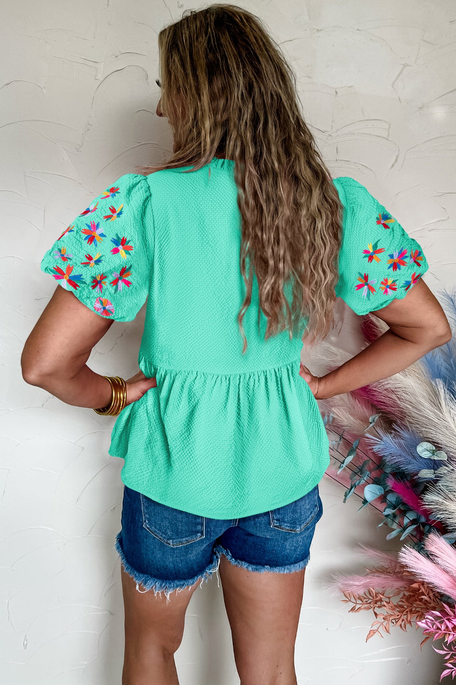 Back view of a mint green puff sleeve blouse with floral embroidery, paired with denim shorts