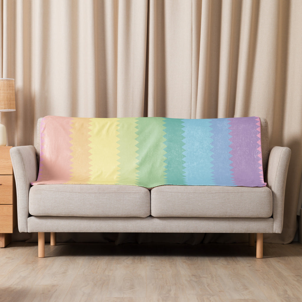 LuckeLadybug rainbow pride sherpa blanket draped over beige sofa with pastel rainbow colors