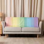 LuckeLadybug rainbow pride sherpa blanket draped over beige sofa with pastel rainbow colors
