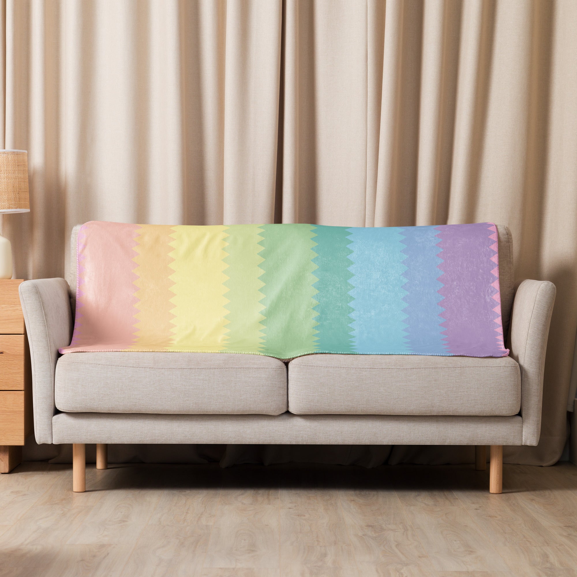 LuckeLadybug rainbow pride sherpa blanket draped over beige sofa with pastel rainbow colors