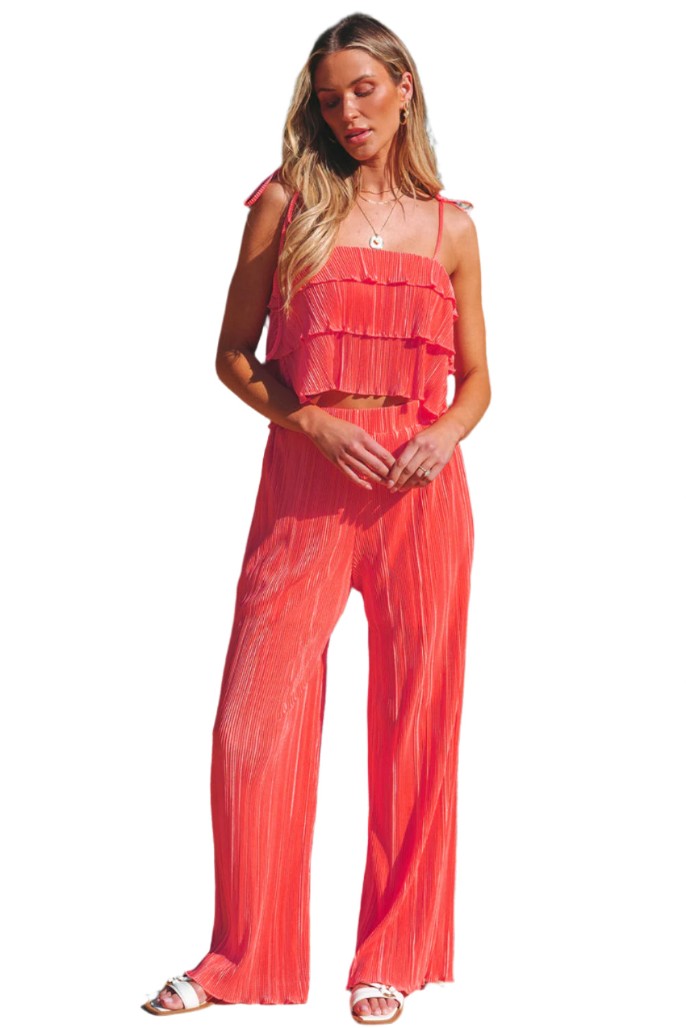 Woman wearing coral ruffle tiered cami pants set standing by pool with tropical plants