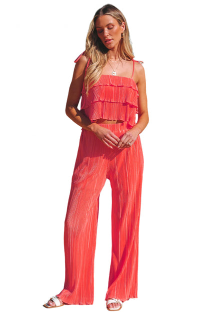 Woman wearing coral ruffle tiered cami pants set standing by pool with tropical plants