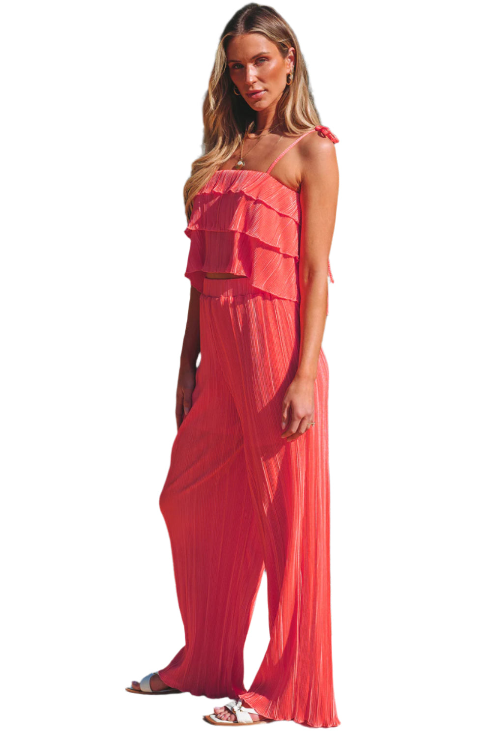 Woman wearing a coral ruffle tiered cami pants set standing by a pool with tropical plants