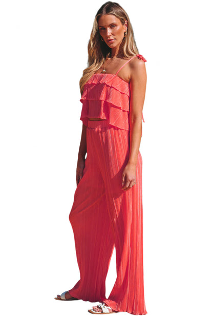 Woman wearing a coral ruffle tiered cami pants set standing by a pool with tropical plants