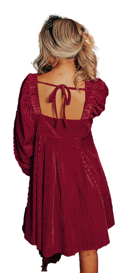 LuckeLadybug model wearing burgundy velvet babydoll dress with open back tie by a Christmas tree black velvet babydoll dress