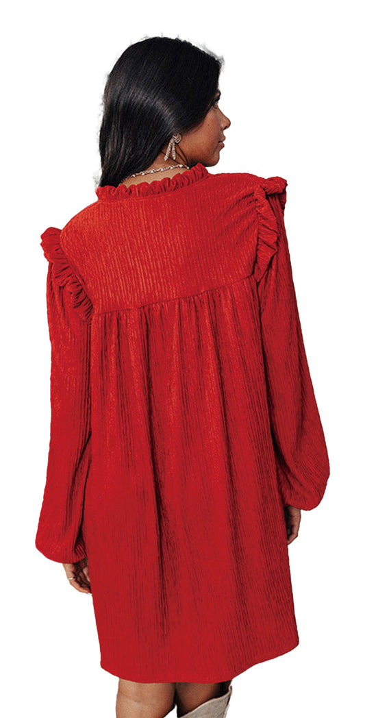 Woman wearing LuckeLadybug fiery red ruffled mini dress back view with long sleeves and ruffle yoke near Christmas tree
