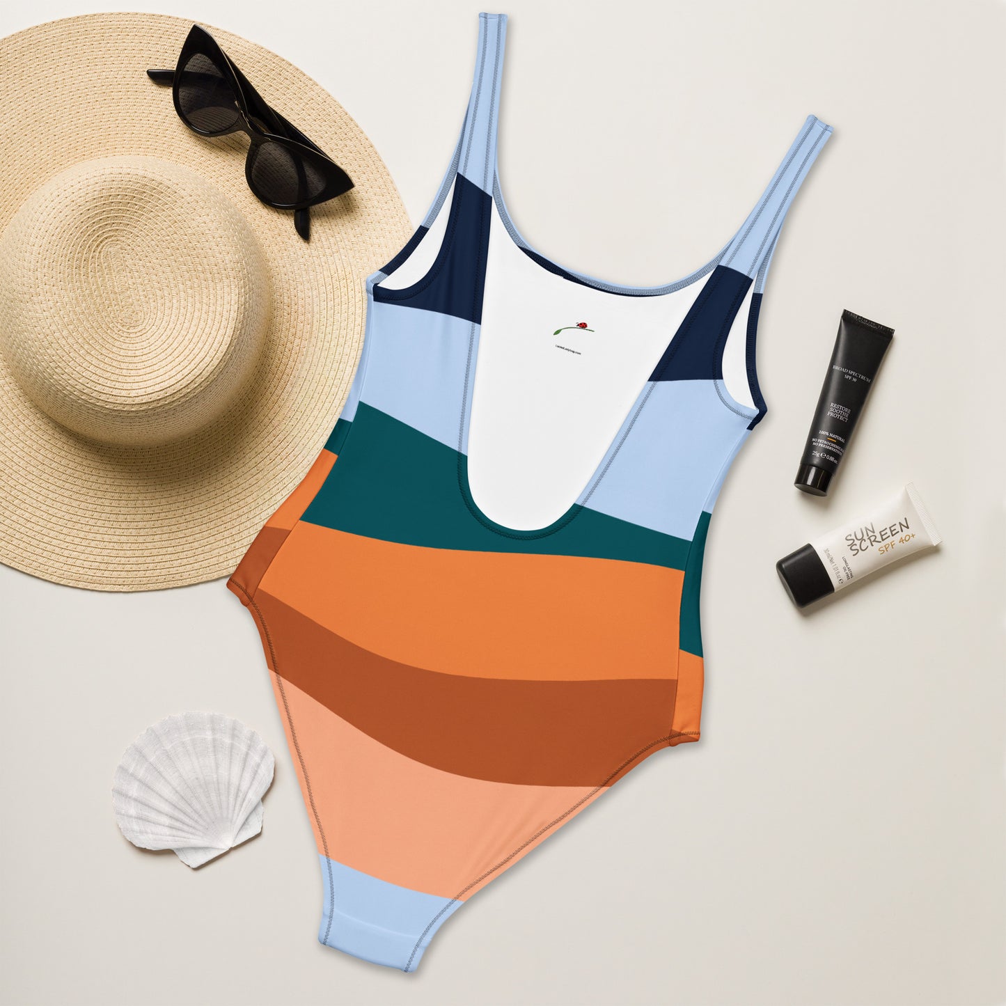 LuckeLadybug elegant striped one-piece swimsuit for women in multicolor retro stripes laid with sunhat sunglasses and sunscreen