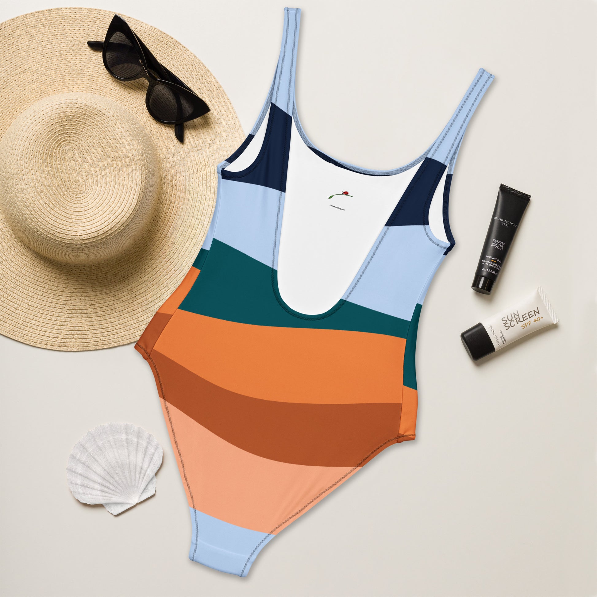 LuckeLadybug elegant striped one-piece swimsuit for women in multicolor retro stripes laid with sunhat sunglasses and sunscreen