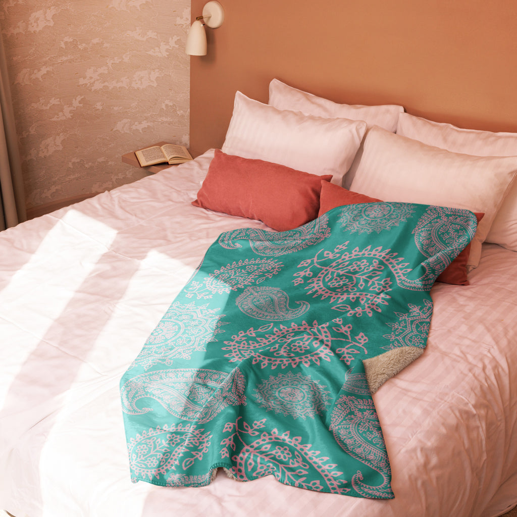Turquoise paisley sherpa blanket draped over bed with white and rust-colored pillows