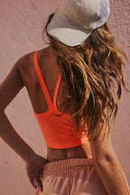 Back view of a woman wearing LuckeLadybug grapefruit orange cropped cami top with a beige cap and pink pants