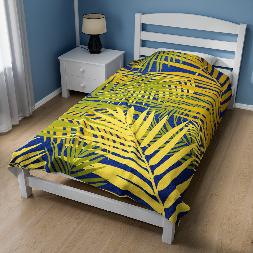 LuckeLadybug tropical palm print blanket with yellow and green leaves on blue background on white bed