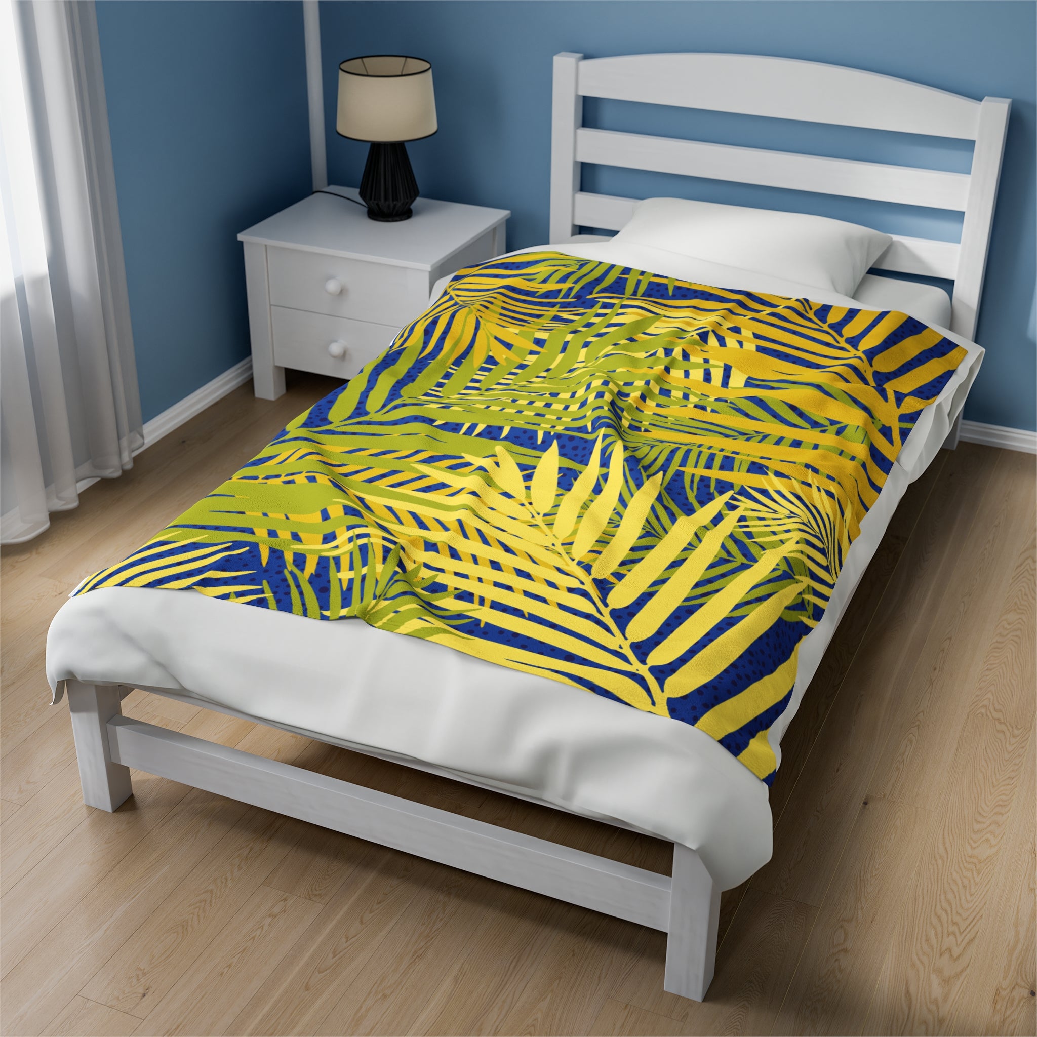 Tropical palm print blanket with bright yellow and green palm leaves on a blue background on a white bed