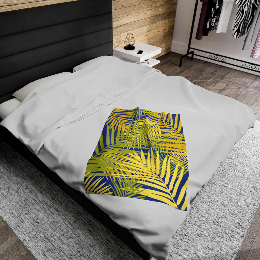 LuckeLadybug tropical palm print blanket with vibrant yellow and blue palm leaves on white bedding