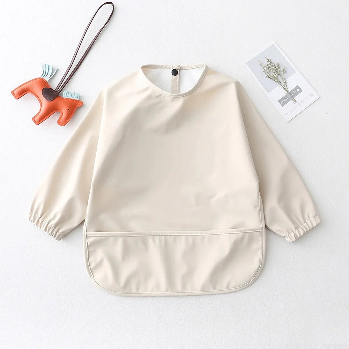 Light beige waterproof baby art smock with elastic sleeves and a front pocket for mess-free creativity