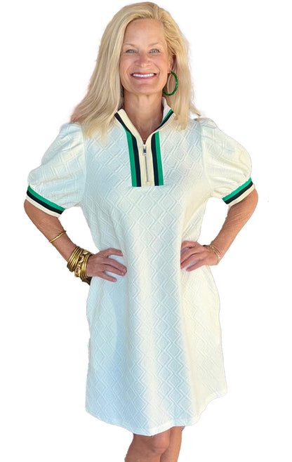 Woman modeling a white jacquard mini dress with green collar accents in a boutique setting