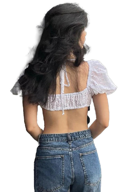 Back view of a woman wearing a white puff sleeve crop top with adjustable ties paired with high-waisted jeans