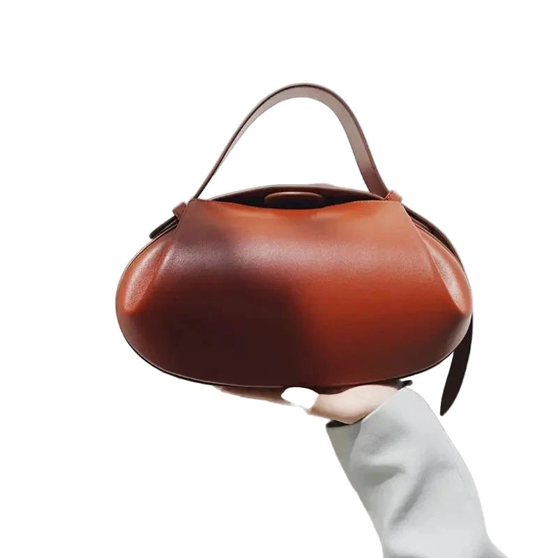 LuckeLadybug LLC women's crossbody round bag in brown held in one hand against a light background