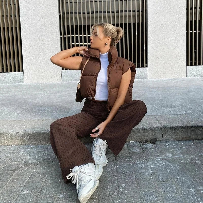 Trendy women's short down vest in brown, styled with high-waisted pants and sneakers for a chic look